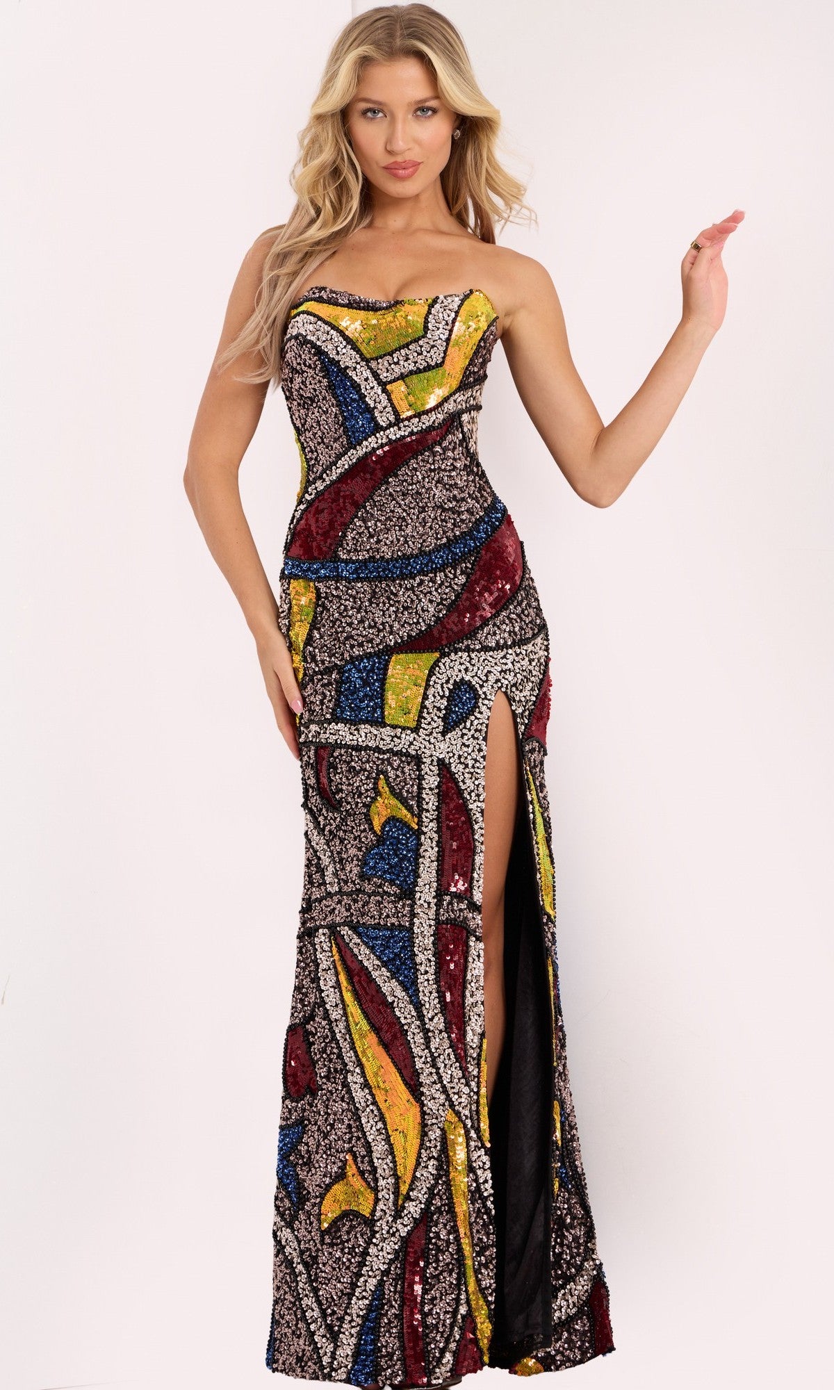 A woman models the Jovani 48617 long prom dress in Multi, featuring a strapless neckline, vibrant abstract mosaic pattern, high side slit, and chic sheath silhouette.